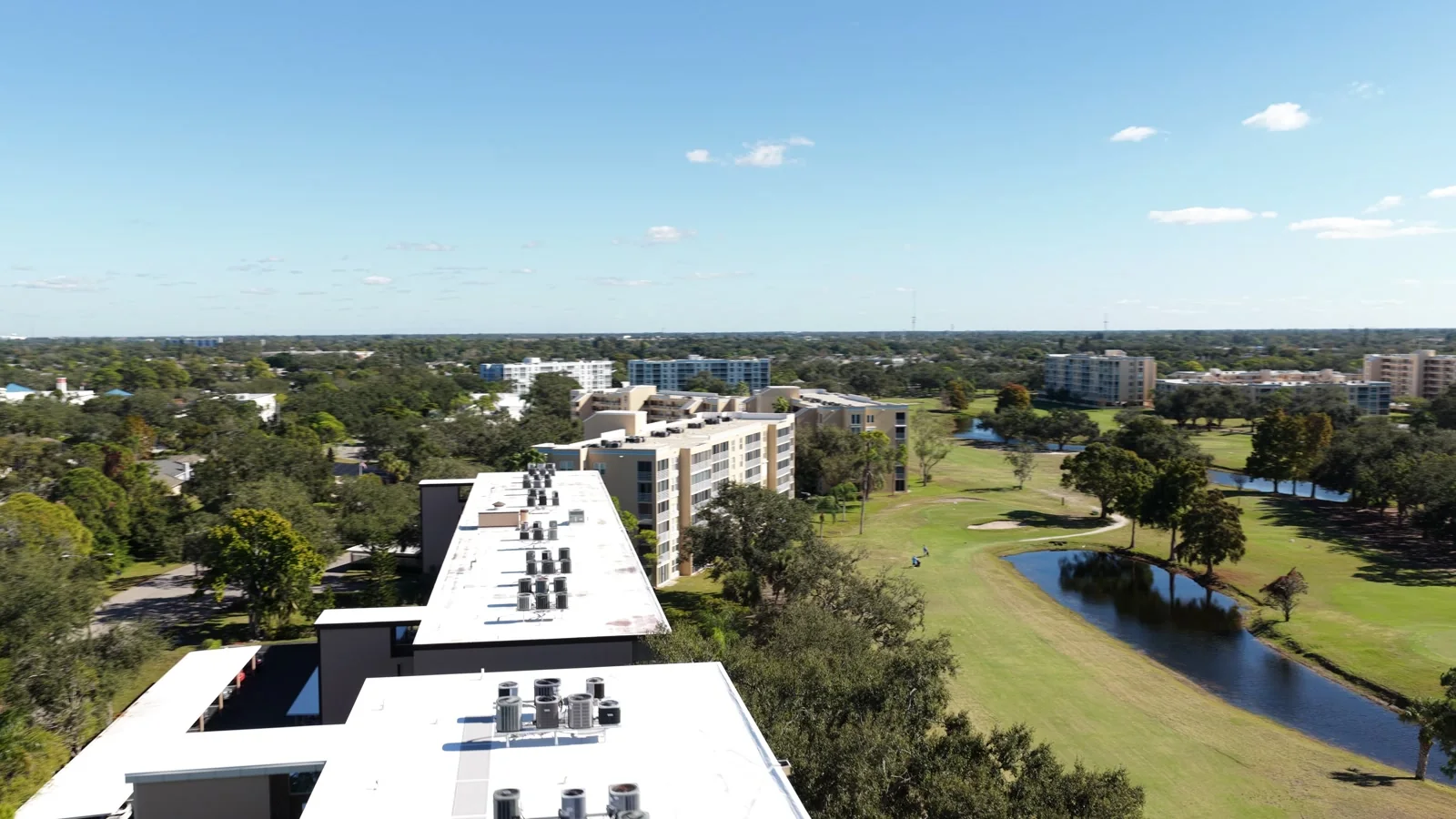 Drone view along a line of flat roofs beside trees and a pond