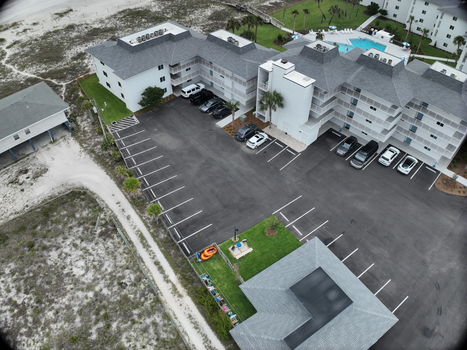 Angled drone view of a condominium roof, parking area and adjacent ground