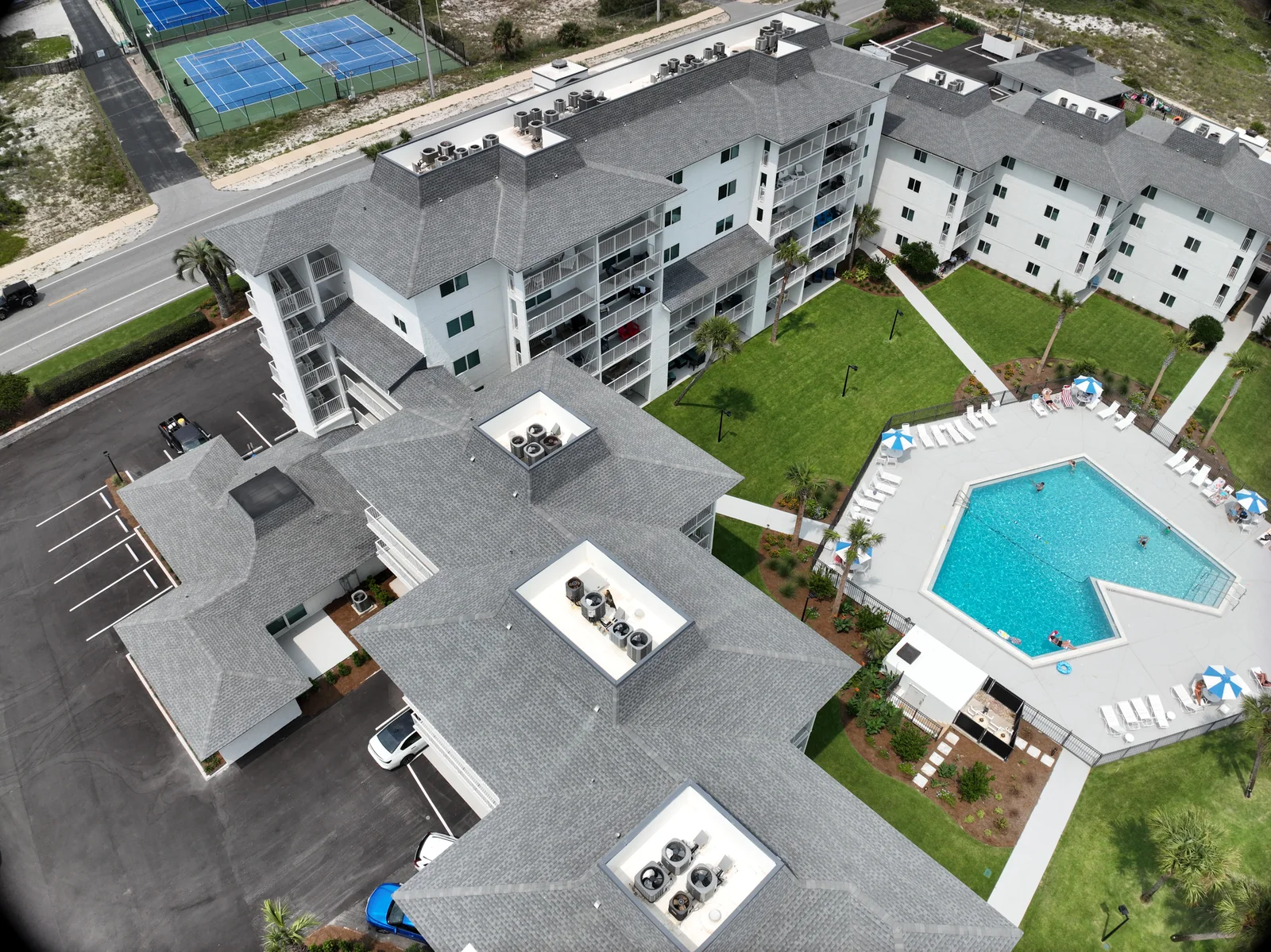 Drone view of condominium roofs, rooftop units and a swimming pool from another angle