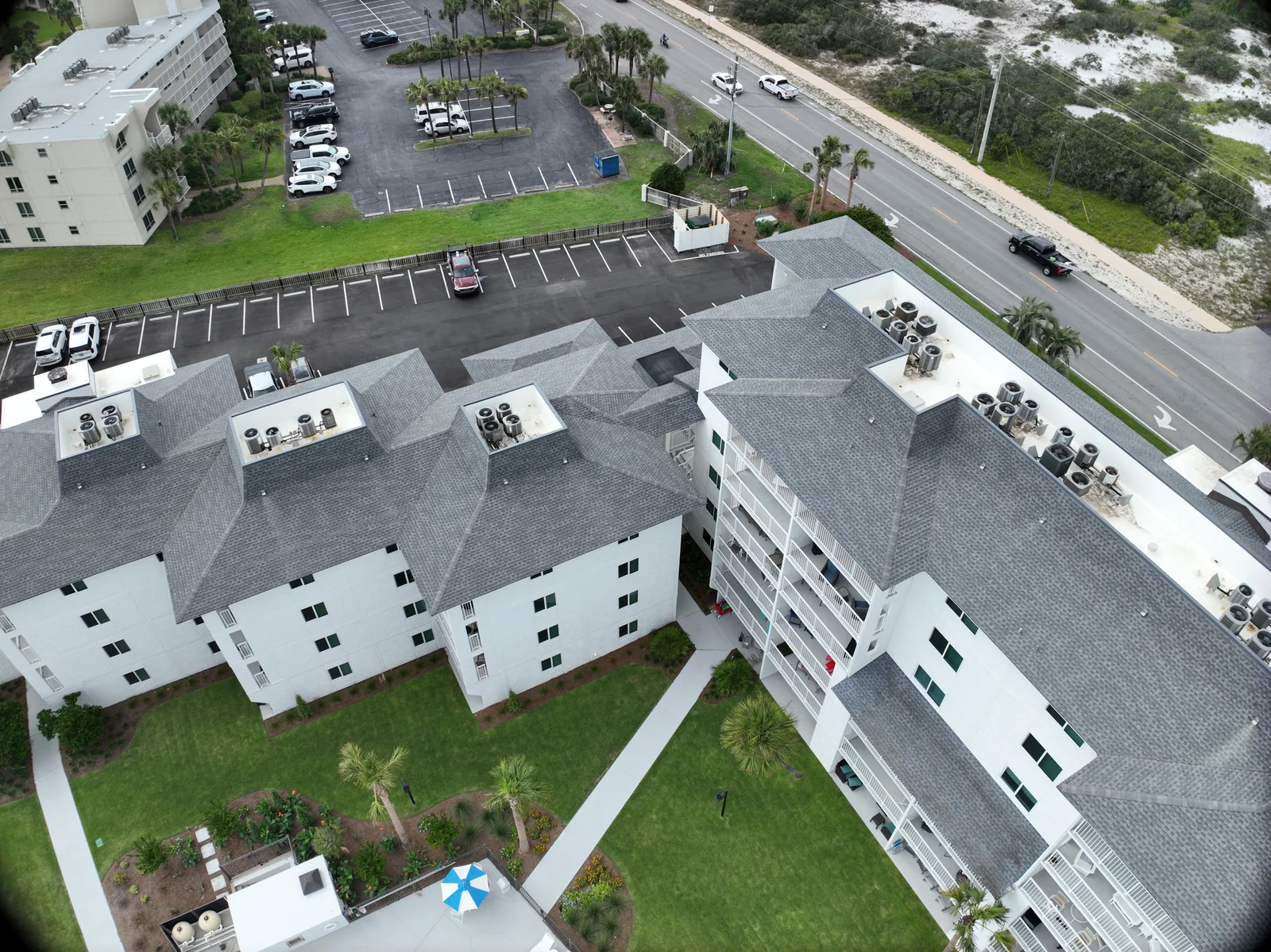 Oblique aerial view across gray condominium roofs toward the adjacent road