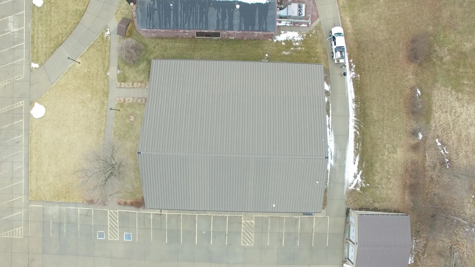 Downward drone view of a large metal roof beside a marked parking area