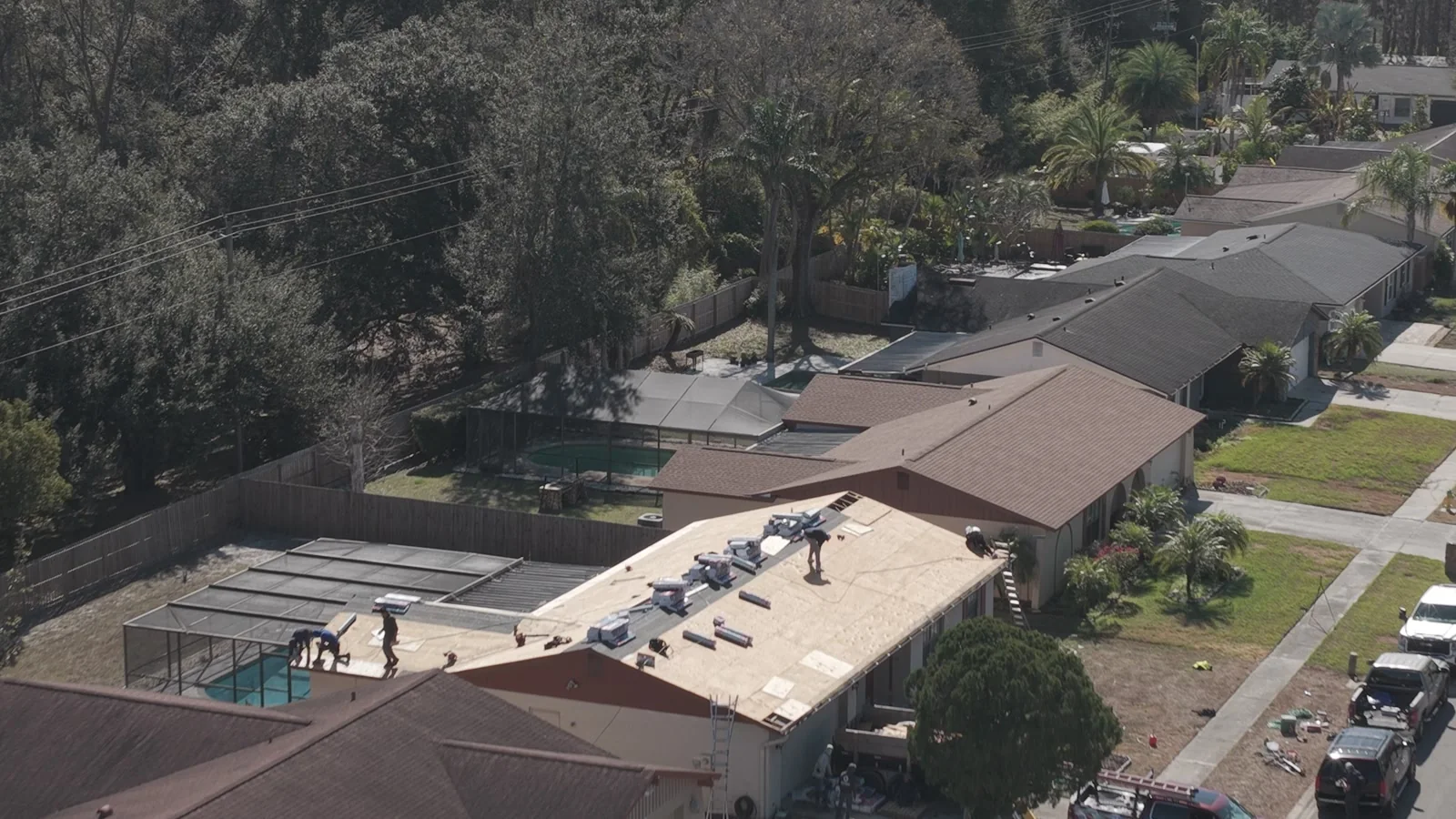 Aerial frame showing an exposed roof deck, workers and arranged roofing materials