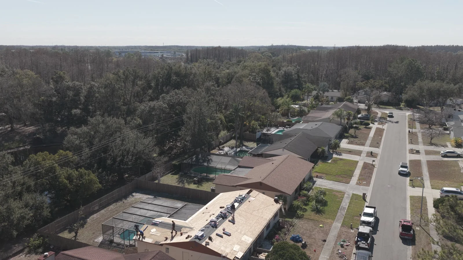 Drone view of an exposed roof with workers and materials within a neighborhood